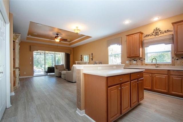 kitchen with a center island, light hardwood / wood-style flooring, a tray ceiling, ceiling fan, and decorative backsplash