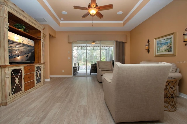 living room featuring crown molding, ceiling fan, a tray ceiling, and light hardwood / wood-style flooring