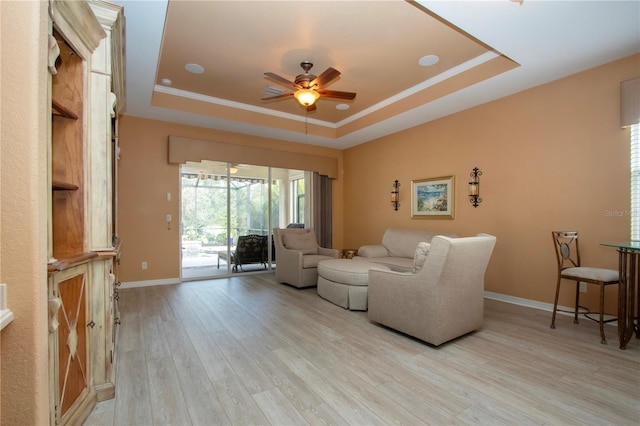 living room with ceiling fan, light wood-type flooring, and a tray ceiling