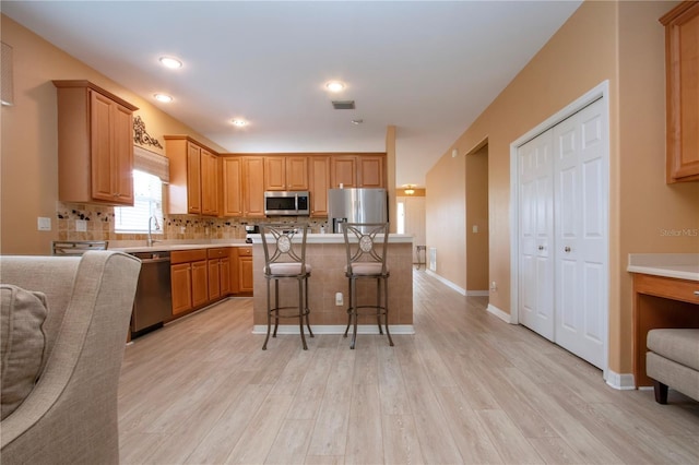 kitchen featuring light hardwood / wood-style flooring, a breakfast bar, appliances with stainless steel finishes, a center island, and decorative backsplash