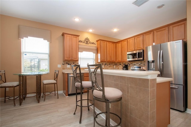 kitchen with stainless steel appliances, a kitchen bar, a kitchen island, and light wood-type flooring