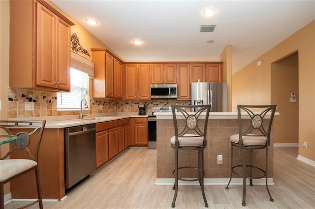 kitchen with sink, a breakfast bar area, light wood-type flooring, a kitchen island, and stainless steel appliances