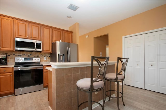 kitchen with a center island, light hardwood / wood-style flooring, appliances with stainless steel finishes, a kitchen breakfast bar, and backsplash