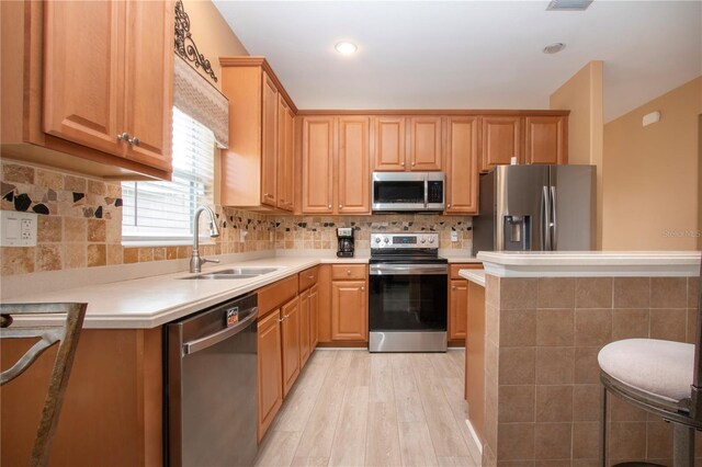 kitchen featuring sink, appliances with stainless steel finishes, a kitchen breakfast bar, light hardwood / wood-style floors, and backsplash