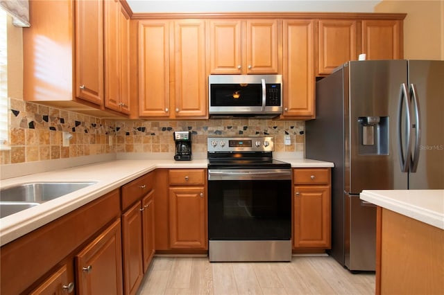 kitchen with stainless steel appliances, sink, backsplash, and light hardwood / wood-style flooring