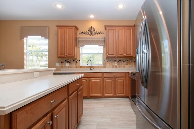 kitchen featuring sink, decorative backsplash, light hardwood / wood-style flooring, and stainless steel refrigerator