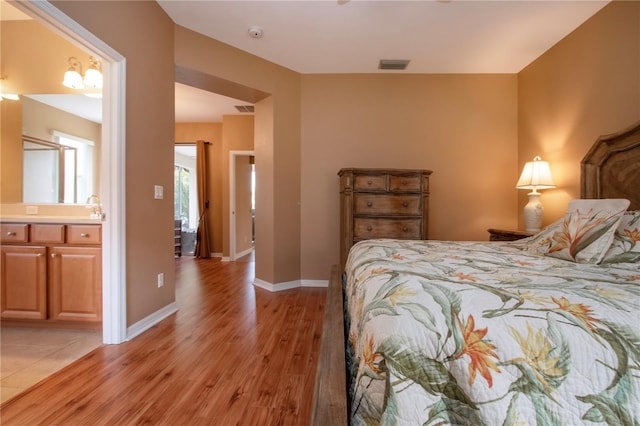 bedroom with ensuite bathroom, sink, and light hardwood / wood-style flooring