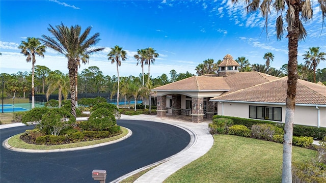 view of home's community featuring a lawn and tennis court