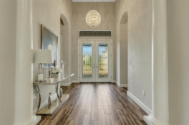 foyer entrance with french doors, an inviting chandelier, wood-type flooring, a towering ceiling, and decorative columns