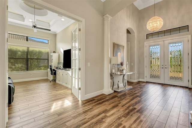 foyer entrance with french doors, ornate columns, crown molding, light wood-type flooring, and a towering ceiling