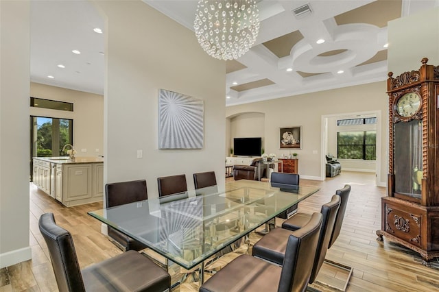 dining space featuring a towering ceiling, coffered ceiling, sink, and light hardwood / wood-style flooring