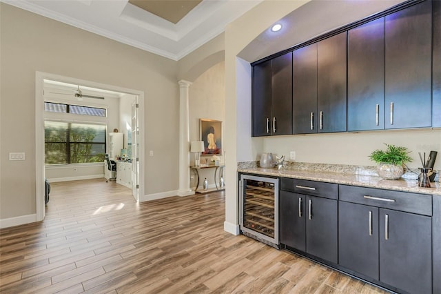 bar featuring dark brown cabinets, light hardwood / wood-style flooring, beverage cooler, light stone countertops, and decorative columns