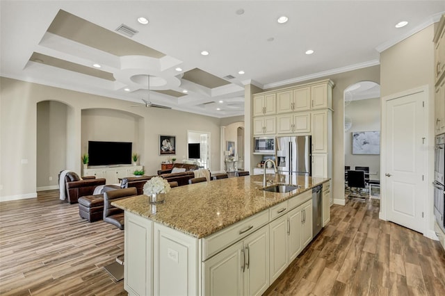 kitchen with sink, a center island with sink, appliances with stainless steel finishes, light stone countertops, and cream cabinets