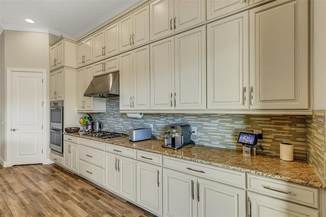 kitchen with appliances with stainless steel finishes, decorative backsplash, ornamental molding, light stone counters, and cream cabinets