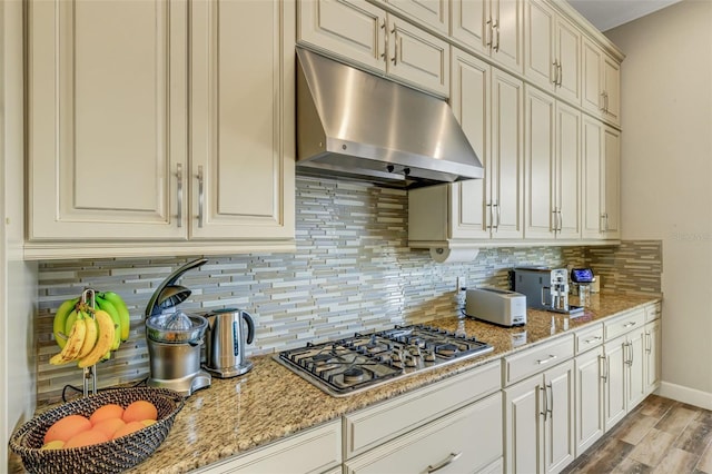 kitchen with stainless steel gas stovetop, tasteful backsplash, light stone counters, and light hardwood / wood-style floors