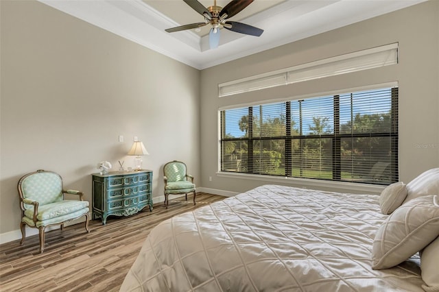 bedroom featuring multiple windows, a tray ceiling, wood-type flooring, and ornamental molding