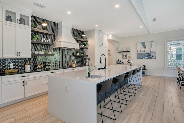 kitchen with premium range hood, a breakfast bar, white cabinetry, sink, and a center island with sink