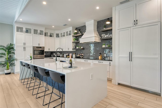 kitchen featuring white cabinetry, sink, an island with sink, and custom range hood