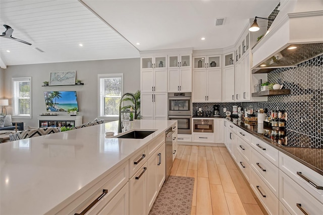 kitchen with sink, custom exhaust hood, white cabinets, and plenty of natural light