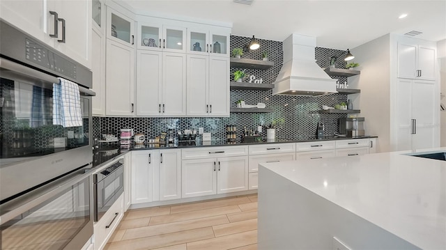 kitchen with premium range hood, stainless steel appliances, decorative backsplash, and white cabinets