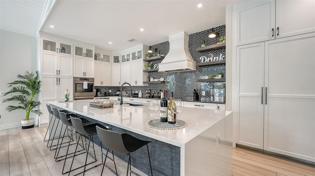 kitchen with a large island, sink, white cabinetry, and custom range hood