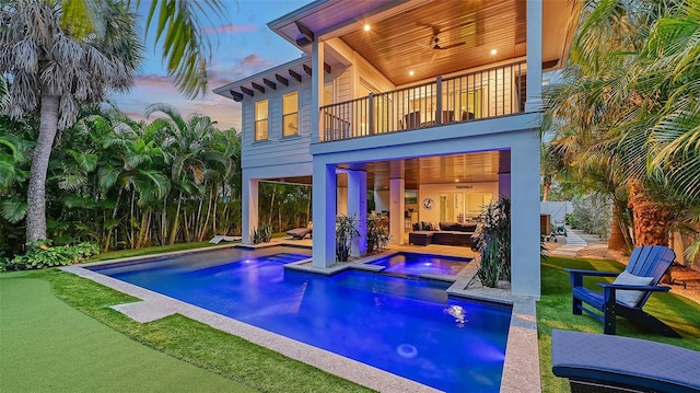 back house at dusk featuring ceiling fan, a patio area, a pool with hot tub, an outdoor hangout area, and a balcony