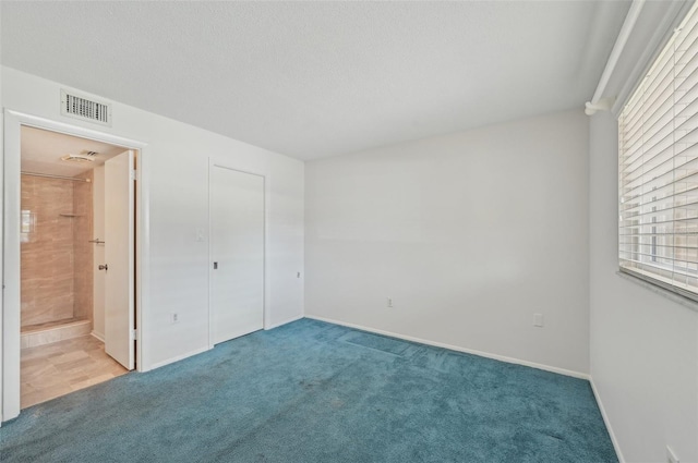 unfurnished bedroom with ensuite bathroom, carpet, and a textured ceiling