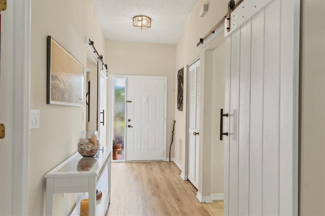 entryway with a textured ceiling, a barn door, light wood-style flooring, and baseboards