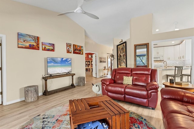 living area featuring a ceiling fan, baseboards, high vaulted ceiling, and light wood finished floors