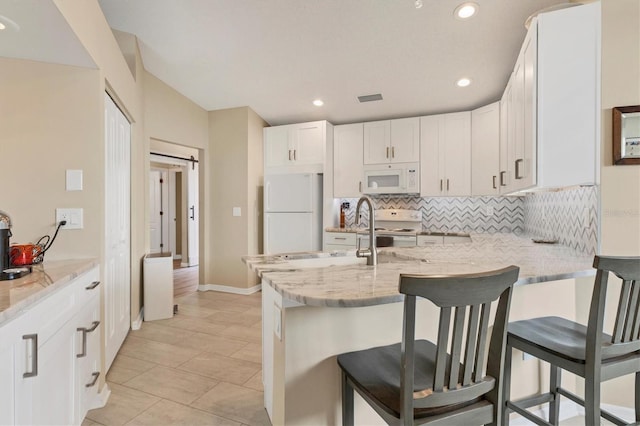 kitchen featuring a peninsula, white appliances, tasteful backsplash, and light stone counters