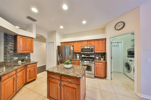 kitchen with light tile patterned flooring, sink, dark stone counters, stainless steel appliances, and washer and clothes dryer