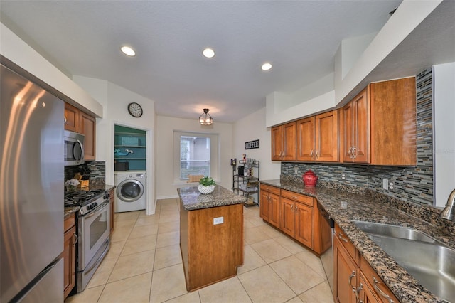 kitchen with sink, a center island, appliances with stainless steel finishes, dark stone counters, and washer / clothes dryer