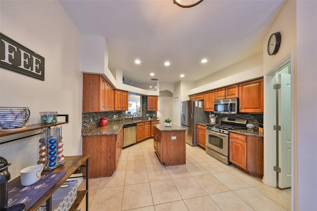 kitchen featuring light tile patterned floors, appliances with stainless steel finishes, a kitchen island, decorative backsplash, and dark stone counters