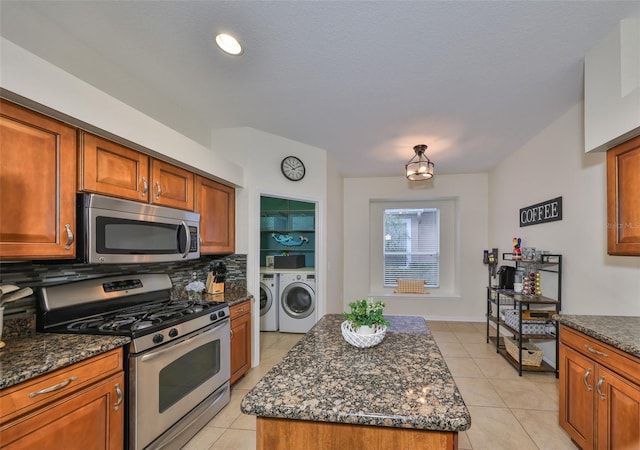 kitchen with light tile patterned flooring, appliances with stainless steel finishes, separate washer and dryer, backsplash, and a center island