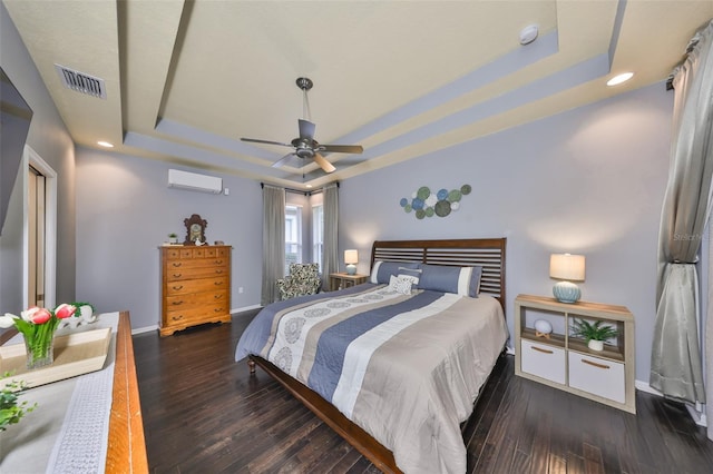 bedroom with a tray ceiling, a wall unit AC, dark hardwood / wood-style floors, and ceiling fan