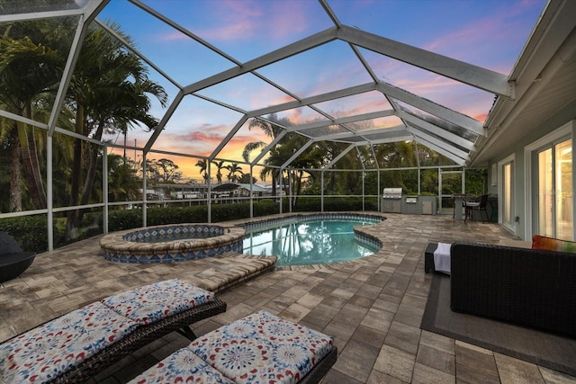 pool at dusk with a patio, glass enclosure, area for grilling, grilling area, and an in ground hot tub