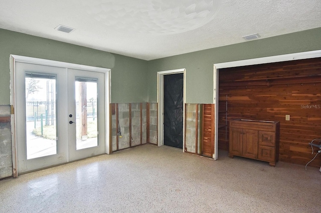 unfurnished bedroom with wood walls, access to exterior, a textured ceiling, and french doors