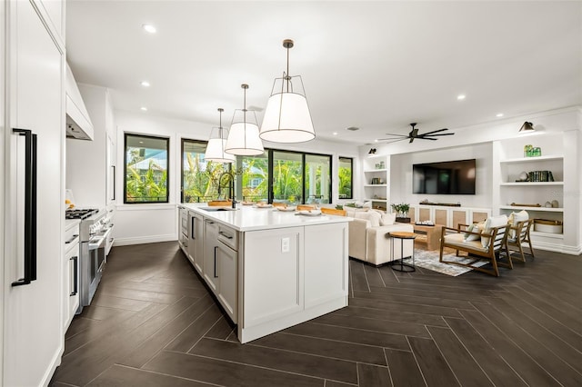 kitchen featuring pendant lighting, high end stainless steel range oven, white cabinetry, dark parquet floors, and a center island with sink