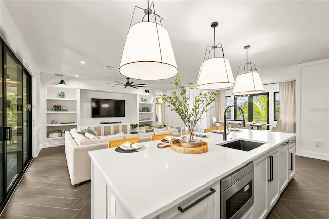 kitchen featuring stainless steel microwave, white cabinetry, pendant lighting, and a center island with sink