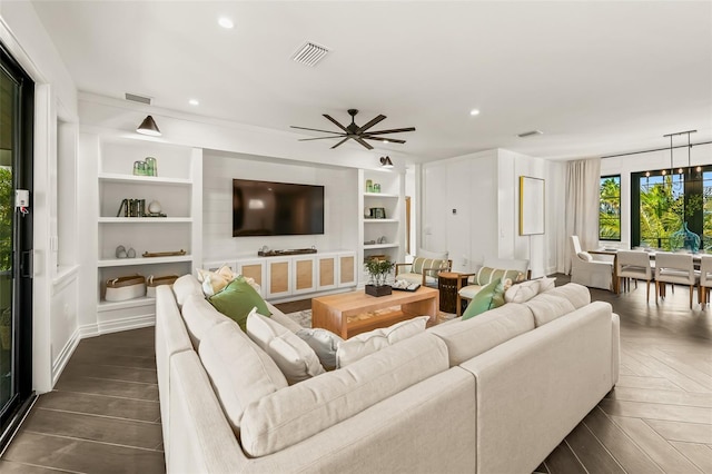 living room with built in shelves, ceiling fan, and dark parquet flooring