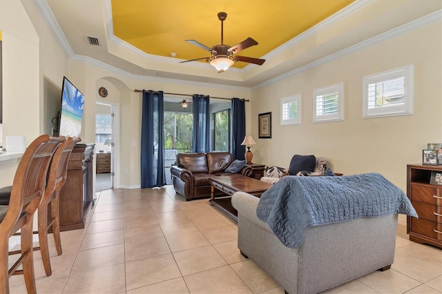 tiled living room with crown molding, ceiling fan, and a raised ceiling