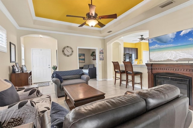 living room with ceiling fan, ornamental molding, a raised ceiling, and light tile patterned floors