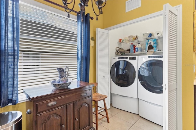 washroom with light tile patterned flooring, washing machine and clothes dryer, and a chandelier