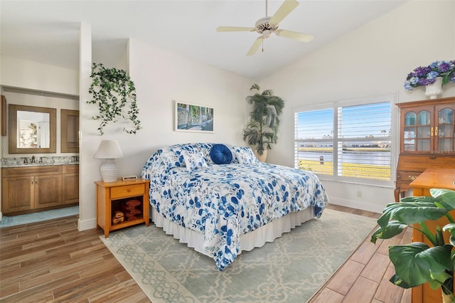 bedroom with lofted ceiling, ceiling fan, a water view, ensuite bathroom, and light wood-type flooring