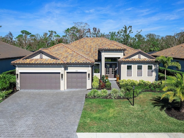 mediterranean / spanish home with an attached garage, a tile roof, french doors, decorative driveway, and a front yard