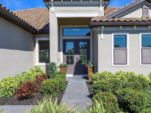 view of exterior entry with french doors, a tile roof, and stucco siding