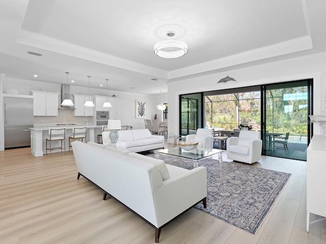 living area with crown molding, a tray ceiling, visible vents, and light wood-style floors