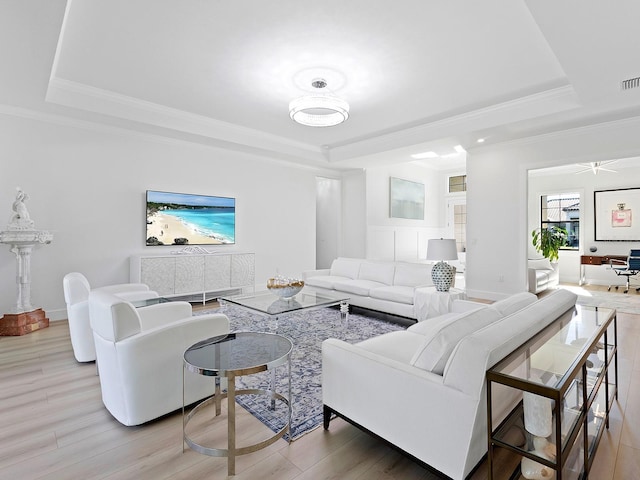 living area featuring ornamental molding, a tray ceiling, light wood-type flooring, and visible vents