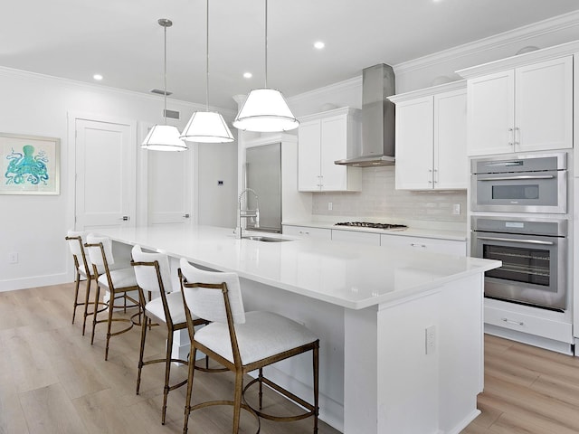 kitchen with pendant lighting, sink, a large island with sink, and wall chimney exhaust hood