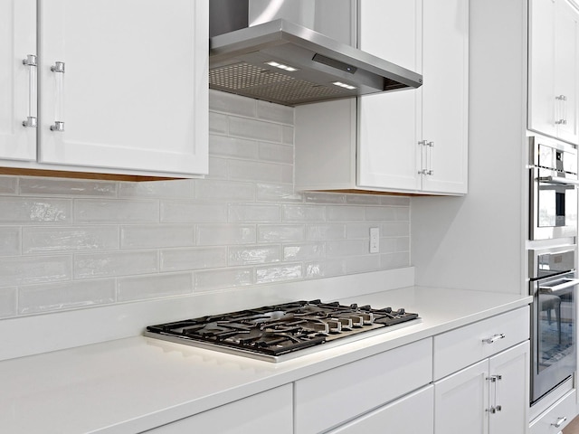 kitchen with stainless steel appliances, wall chimney range hood, and white cabinetry